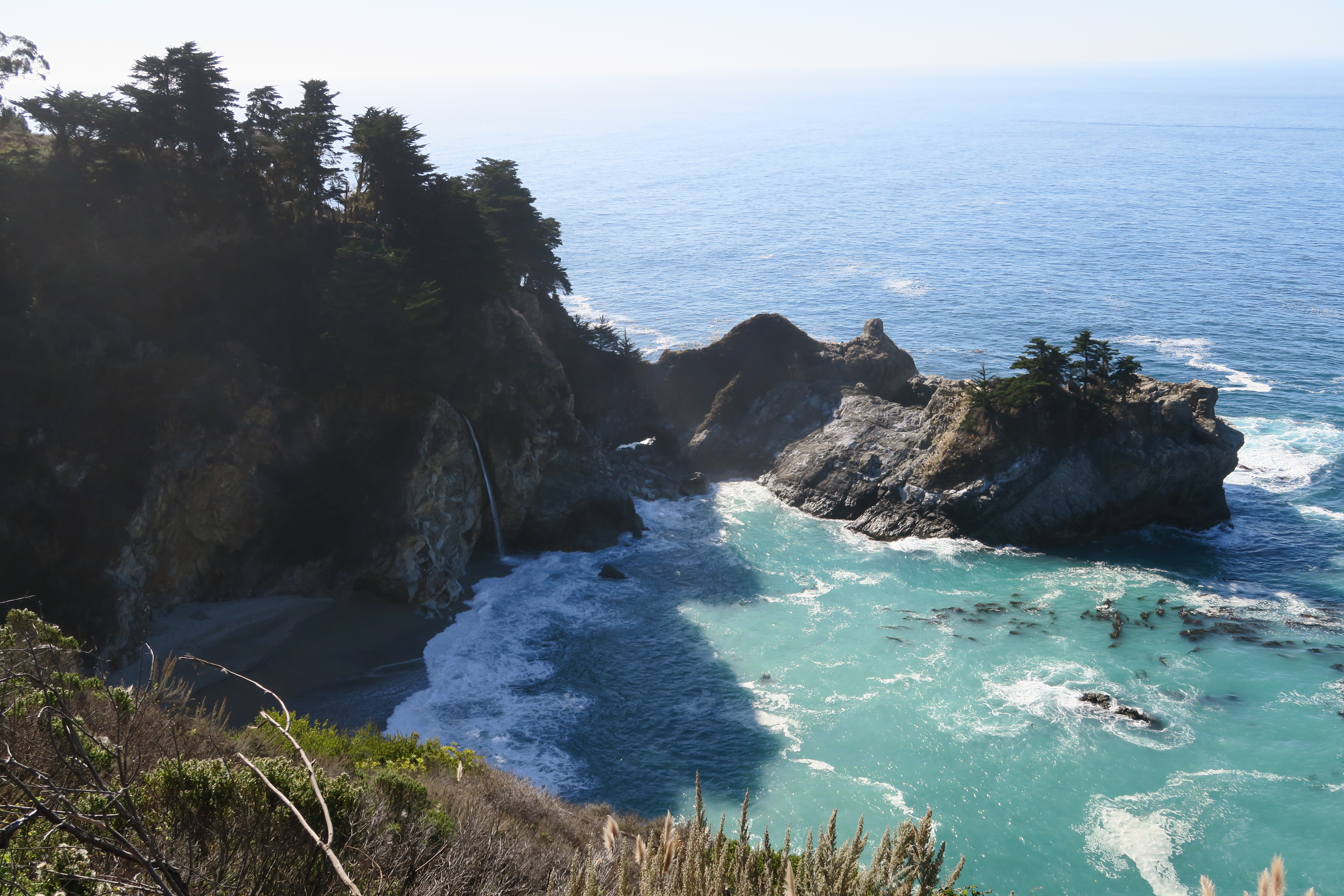 A top-down view of Mcway Falls, with a pristine turquouse blue beach lagoon, surrounded on all sides by rocky cliffs.